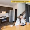 A woman is using a tablet in a modern kitchen with wooden cabinets and a stainless steel refrigerator. Produktbild-Vorschau