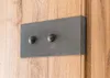 A close-up view of a decorative metal plate with two knobs attached to a wooden surface. Produktbild-Vorschau