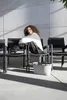 A woman sits on a chair outdoors, with a shopping basket in front of her. Produktbild-Vorschau
