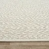 A close-up view of a textured beige rug with a geometric pattern, resting on a wooden floor. Náhled obrázku produktu
