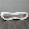 A white, curved bench-like object is placed on a dark wooden floor in front of a textured gray wall. Produktbild-Vorschau
