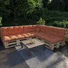 An outdoor patio with a sectional sofa made of pallets and orange cushions, a coffee table, and a rug. Voir les images du produit