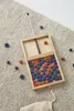 A wooden game board with colorful pieces scattered on a textured carpet. Produktbild-Vorschau