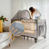 A woman is looking into a baby crib/playpen in a living room setting. Produktbild-Vorschau