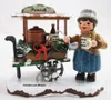 A wooden figurine of a woman selling punch from a cart in the snow. Produktbild-Vorschau