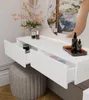 A close-up view of a white vanity table with two open drawers, a gray upholstered stool, and decorative items on top. Produktbild-Vorschau