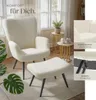 A cream-colored armchair and ottoman set in a cozy living room setting with plants and side tables. Náhled obrázku produktu