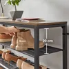 A hand is shown adjusting a shoe on a multi-tiered shoe rack. The shoe rack is made of wood and metal. There are several pairs of shoes on the lower shelves. Náhled obrázku produktu