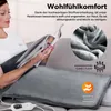 A woman is relaxing on a couch reading a magazine while a heating pad is placed on her lap. Produktbild-Vorschau