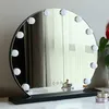 A round makeup mirror with lights on a black stand, placed on a white surface. Produktbild-Vorschau