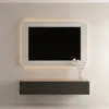 A modern TV board with a floating design, featuring a dark gray cabinet and a light wood top, mounted on a textured light gray wall. A minimalist TV with a glowing frame is mounted above it, and a small vase with white flowers sits on the right side of the Produktbild-Vorschau