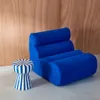 A blue armchair and a striped stool against a wood-paneled wall. Produktbild-Vorschau
