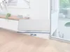 A white mop pad is placed on a light-colored wooden floor in front of a white cabinet and a large window. Produktbild-Vorschau