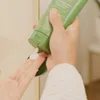 A person is squeezing a green tube of lotion onto their palm. Anteprima dell’immagine prodotto