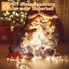 Two children wearing Santa hats are sitting on the floor, surrounded by Christmas lights and a Christmas tree in the background. Produktbild-Vorschau