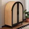 A wooden cabinet with black trim and rattan doors, placed indoors next to a plant. Produktbild-Vorschau