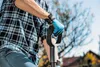 A person wearing gardening gloves and a plaid shirt holds the handle of a shovel outdoors. Náhľad obrázku produktu