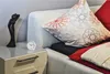 A close-up view of a bedside table next to a bed, featuring a clock and a decorative figurine. Anteprima dell’immagine prodotto
