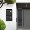 A modern house entrance with a grey door, a glass panel, and two black mailboxes mounted on a white wall. A green bush is in the foreground, and a tree branch is visible at the top. Produktbild-Vorschau