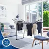 A drying rack with clothes is set up in a bright, modern living room with a large sliding glass door leading to an outdoor patio. Produktbild-Vorschau