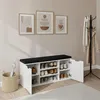 A shoe cabinet with a bench seat in a hallway, with artwork on the wall and a coat rack in the background. Náhľad obrázku produktu