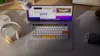 A desk setup with a laptop, keyboard, headphones, and a game console. Produktbild-Vorschau