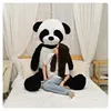 A person sitting on a bed next to a large stuffed panda. Produktbild-Vorschau
