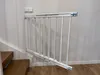 A white metal baby gate is installed at the top of a wooden staircase. Voir les images du produit