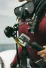 A close-up of a scuba diver wearing a maroon wetsuit and a GoPro camera attached to their gear. Voir les images du produit