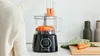 A person is using a black Bosch food processor to slice carrots. Produktbild-Vorschau