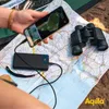 A person is using a smartphone connected to a power bank while looking at a map and binoculars, suggesting an outdoor or travel scenario. Produktbild-Vorschau