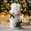 A stack of three illuminated gift boxes decorated with pine cones, pine needles, and red berries, set against a blurred background of a Christmas tree with lights and other wrapped gifts. Anteprima dell’immagine prodotto