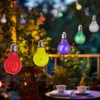 A string of colorful LED light bulbs hanging outdoors at night, with a table and chairs in the foreground. Produktbild-Vorschau
