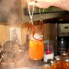 A person is using jar tongs to lift a jar of orange jam out of a pot of steaming water. Produktbild-Vorschau