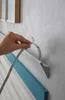 A hand is shown peeling the backing off a strip of LED lighting to attach it to a wall. Produktbild-Vorschau