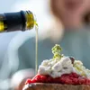 Olive oil being poured from a bottle onto a dish of food. Produktbild-Vorschau