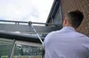 A person is cleaning the exterior of a building with a long-handled cleaning tool. Produktbild-Vorschau