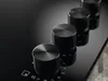 A close-up shot of four black control knobs on a black induction hob. Voir les images du produit