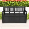 A black storage bench is placed outdoors on a patio, with lush green foliage and red flowers in the background. Produktbild-Vorschau