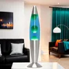 A lava lamp is shown in a living room setting with a sofa and curtains. Produktbild-Vorschau