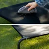 A person is cleaning a black elevated dog bed with a cloth, and another shot shows the dog bed on grass. Náhled obrázku produktu