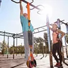 An older man is using a pull-up assist band on an outdoor fitness equipment setup, while a woman watches. Anteprima dell’immagine prodotto