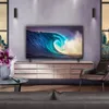 A modern living room with a large TV displaying a wave, a wooden media console, a leather armchair, and a coffee table with a flower vase and remote. Voir les images du produit
