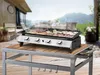 A gas griddle with food cooking on it, placed on a table outdoors on a deck. Náhled obrázku produktu