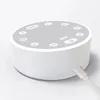 A white, round baby sleep sound machine with a gray top featuring several buttons and a USB-C charging port on the side. Produktbild-Vorschau
