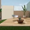 An outdoor patio scene with a beige privacy screen, a white chair, and a coffee table with decorative items. Produktbild-Vorschau