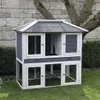 A multi-level wooden hutch for small animals, set up outdoors on a grassy lawn. Voir les images du produit