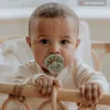 A close-up shot of a baby holding onto a crib railing, with a pacifier in its mouth. Produktbild-Vorschau