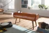 A brown leather bench with wooden legs sits on a wooden floor in a room with stairs and a window. Náhľad obrázku produktu