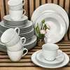 A set of white porcelain dishes and cups with a subtle pattern and gray trim, arranged on a wooden surface. Produktbild-Vorschau